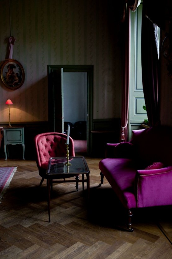 a modern Gothic living room with pritned wallpaper, paneled walls, jewel-tone furniture, touches of green and moody artworks