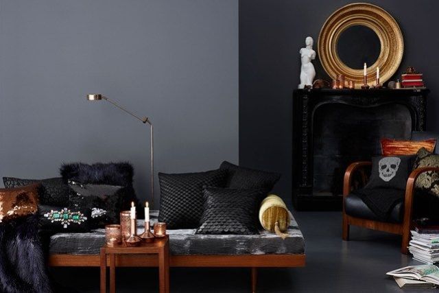 a modern Gothic living room with grey walls, a black statement wall with a fireplace, candles, a mirror in a gold frame, a sofa and bold and black pillows