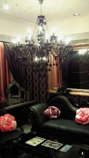 a chic Gothic living room with statement mirrors, refined black furniture, a black chandelier, pink pillows and printed wallpaper