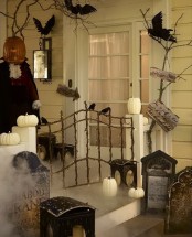 a Halloween porch turned into a graveyard with blackbirds, pumpkins and pumpkin candles, branches and a ghost dressed in a costume