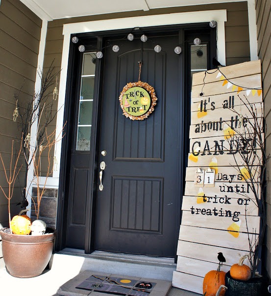 a simple and casual Halloween front door styled with a plaque sign, branches, pumpkins, skulls and a large planked sign