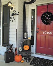 a Halloween front porch decorated with orange pumpkins, a black cat head, a witch’s broom, spiders and a black wreath with googly eyes
