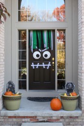 a Halloween front door turned into a monster and planters with pumpkins and black tombstones is a cool idea for this celebration