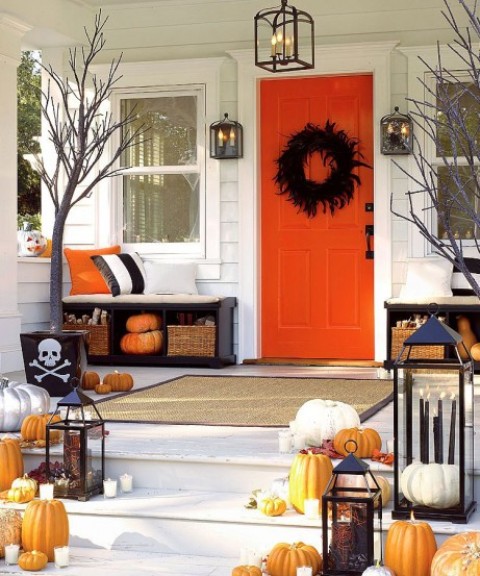 a cozy rustic Halloween porch done with fall leaves and pumpkins, with branches and candle lanterns, a black feather wreath is a lovely solution