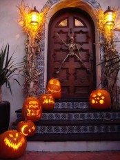 a Halloween porch decorated with jack-o-lanterns, corn husks and a skeleton right on the door is a unique idea