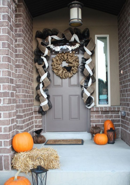 a Halloween front porch with pumpkins, hay, candle lanterns, a burlap wreath and burlap garland over the door