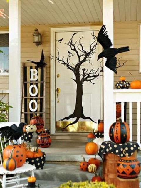 a bold Halloween porch with orange, black and white painted pumpkins, a silhouette tree on the door, blackbirds and black letters, a witch hat and a witch broom
