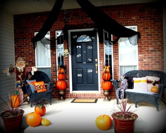 a Halloween front porch with black wicker furniture, pumpkins and planters, eyes on the door and black fabric over the door
