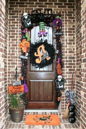 a colorful Halloween front door with black, purple, green and orange decor, a garland, lights, tombstones and witches’ parts is a fun idea