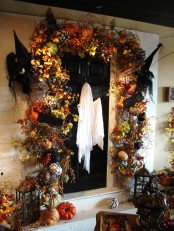 a crazy Halloween front door decor with bright faux leaves, pumpkins, twigs, nests, witches’ hats and candle lanterns on each side on the door