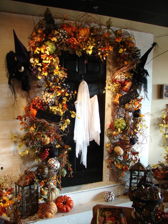 a crazy Halloween front door decor with bright faux leaves, pumpkins, twigs, nests, witches' hats and candle lanterns on each side on the door