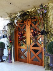 an outstanding and bold Halloween front door done with green twigs, oversized black spiders, ghosts, cats and striped stockings is a playful solution