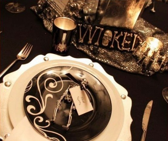 a stylish black and white Halloween party table with contrasting plates, candles, silver candleholders and a runner and a sign is very cool