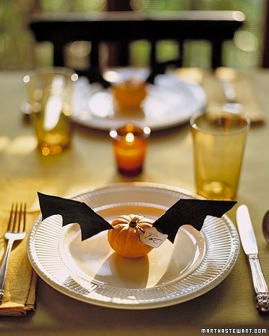 a cozy rustic Halloween tablescape with white plates, silver cutlery, mustard glasses, orange candles, pumpkins with bat wings