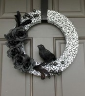 a black and white Halloween wreath with a printed form, black faux blooms and berries and a faux blackbird is a gorgeous idea