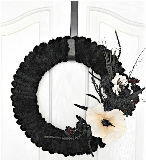a refined black faux fur Halloween wreath with black faux blooms, grasses and leaves plus a single white flower is a very elegant idea