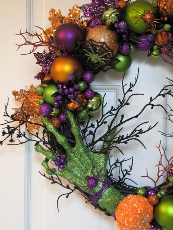 a colorful Halloween wreath of vine, green, purple, orange ornaments of various sizes, soem glitter twigs, a green skeleton hand and some glitter pumpkins