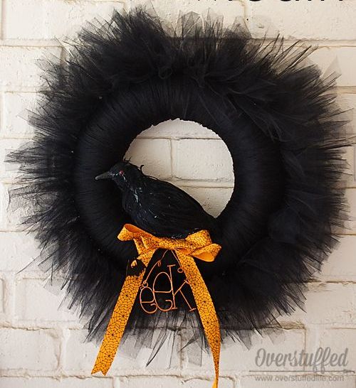 a black Halloween wreath with much black tulel around, with a faux blackbird and an orange bow plus some letters is a stylish decoration for Halloween
