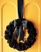 a Halloween wreath covered with black and deep red fabric flowers, with a black ribbon bow on top is lovely