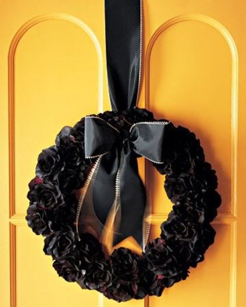 a Halloween wreath covered with black and deep red fabric flowers, with a black ribbon bow on top is lovely