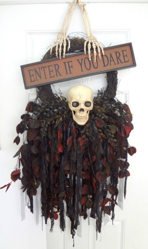 a Halloween wreath of vine, with ribbons, leaves, feathers, a skull and skeleton hands plus a sign on top