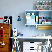 a pastel blue craft and working space with a trestle desk, a file cabinet, a stained cabinet with drawers and box shelves is a cool space