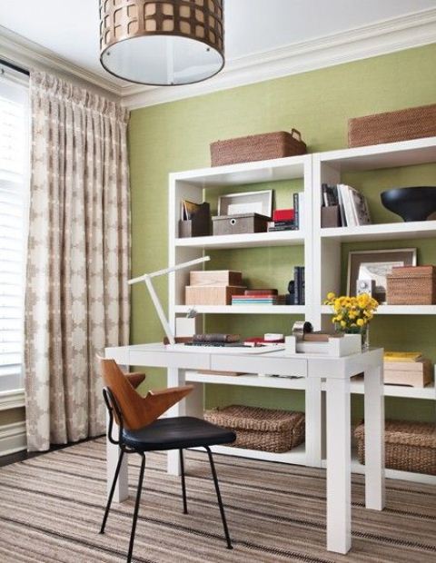 a green home office with a duo of white storage units, a white desk, a black chair and printed textiles and a pendant lamp