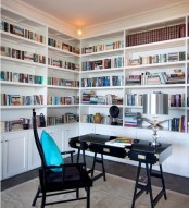 a home office with two walls taken by large bookcases and additional low cabinets, a black desk and a chair, a bold blue pillow is very cool for working