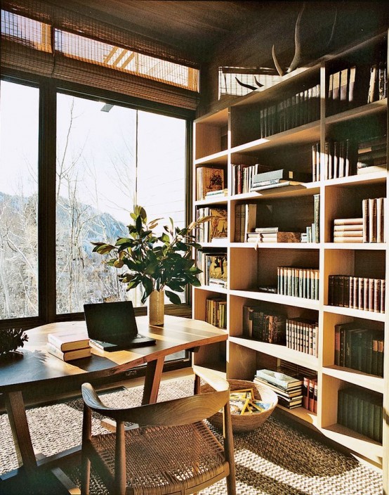 a modern home office clad with light-stained wood, with a glazed wall and a view, an oversized bookcase, a stylish desk and a wooden chair is cozy and welcoming
