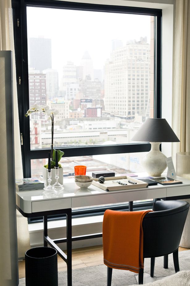 a modern home office with a window and a view of the big city, a white desk, a black chair and a table lamp can be used for makeup and for working
