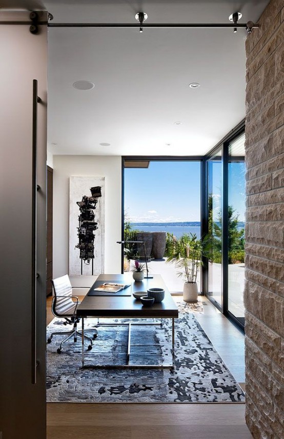 a fab tropical home office with glazed wall that offer a view of a gorgeous scenery, a modern desk, a chair, a rug and an abstract artwork