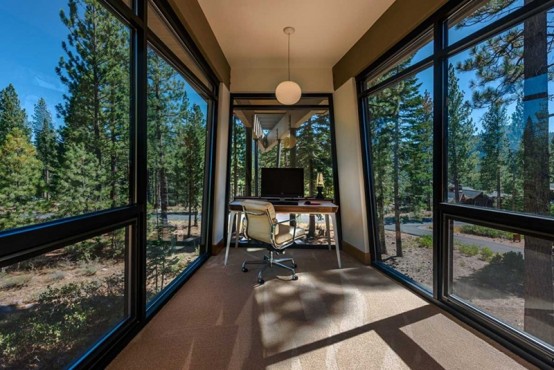 a small yet gorgeous home office with glazed walls that offer lovely forest views, a desk and a chair, a pendant lamp to enjoy the scenery
