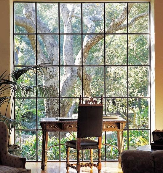 a vintage-inspired home office with a large glazed wall, a vintage desk and a chair, vintage chairs, potted plants and a view of the garden