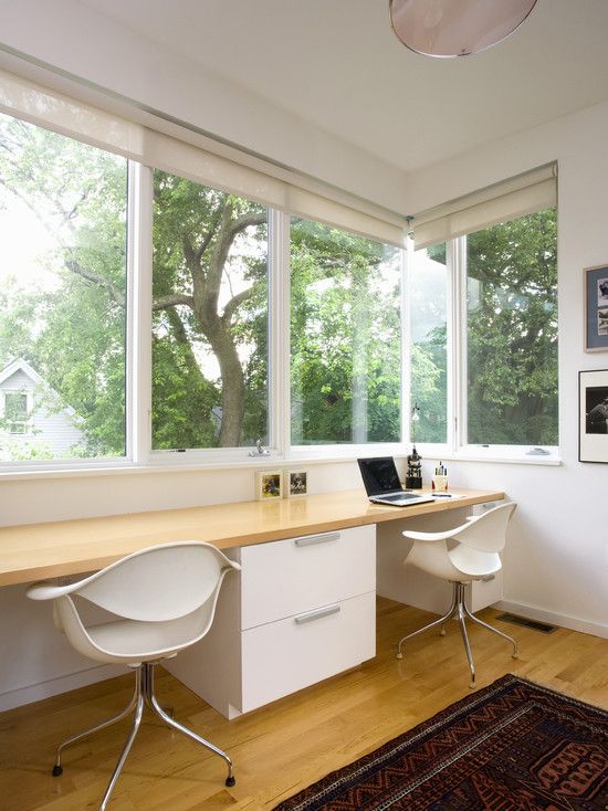 a neutral contemporary home office with a glazed wall and a shared desk, white chairs, a gallery wall and a view of greenery outside