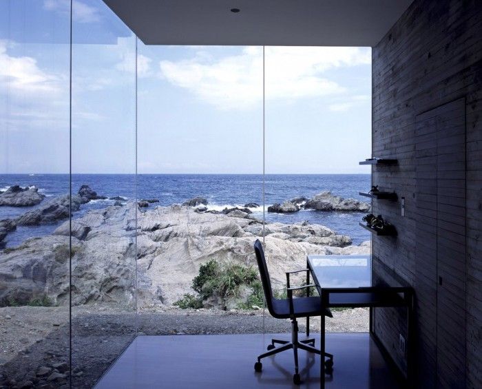 a beautiful small home office with glazed walls, a wall mounted desk and a chair and jaw dropping views of the sea that take the central place here