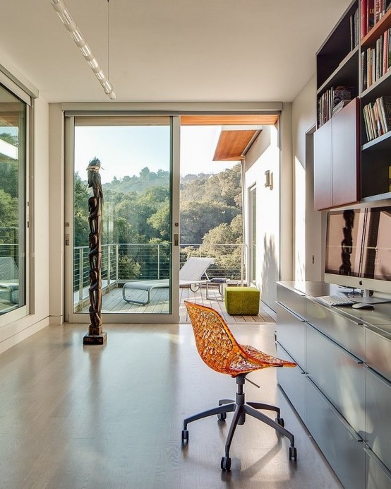 a modern home office with glazed walls and doors, a bookcase and a dresser, a chair and fantastic views of the forest outside that creates a mood and impression here