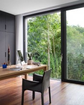 a stylish contemporary home office with a glazed wall, a sliding door that allows entrance to the garden, black sleek storage units, a large desk and a chair