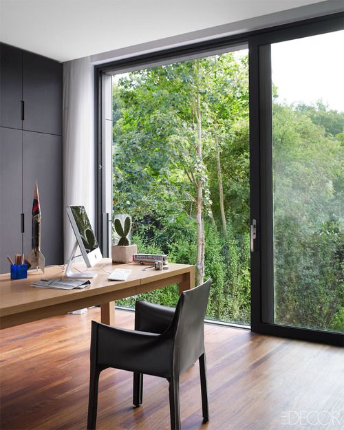 a stylish contemporary home office with a glazed wall, a sliding door that allows entrance to the garden, black sleek storage units, a large desk and a chair