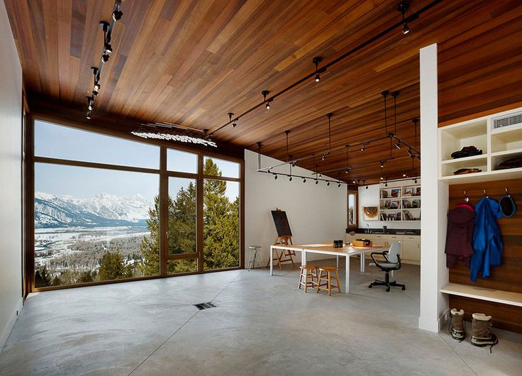 a large chalet home office with glazed walls, mountain views, a desk and chairs, some wall mounted shelves is a beautiful and unique space