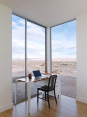 a small and lovely home office with glazed walls that offer views of the desert, a small white desk and a black chair is a lovely space to be in