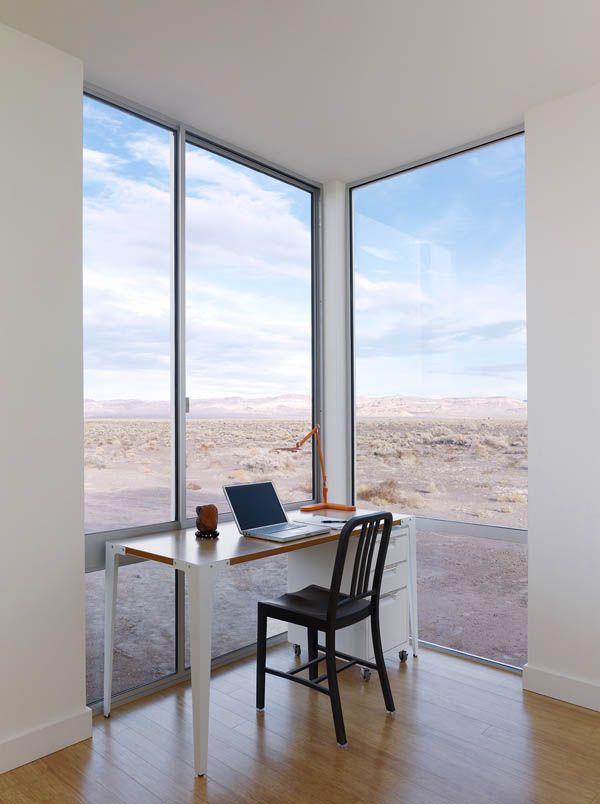 a small and lovely home office with glazed walls that offer views of the desert, a small white desk and a black chair is a lovely space to be in