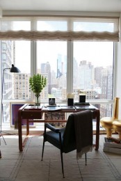 an eye-catchy home office with a glazed wall and big city views, a modern desk and a dark chair, artwork and lamps is a creative space that inspires