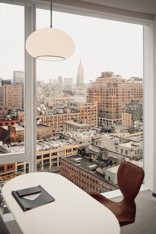 a laconic home office with a glazed wall that allows views of the big city and a white chair and a table - nothing here distracts from the views