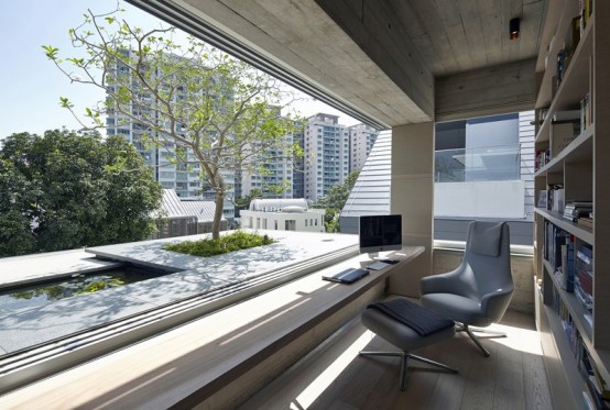 a neutral contemporary home office clad with grey wood, with a large bookcase, a windowsill desk and a window with a view plus a comfy grey chair and a footrest