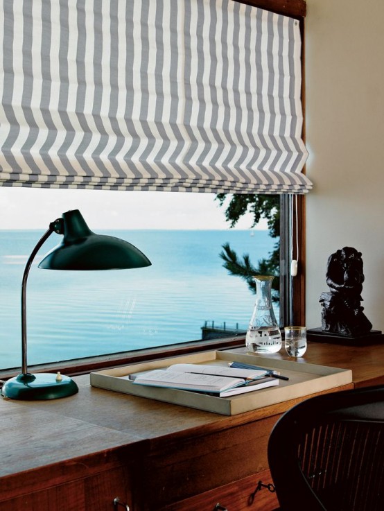 a lovely home office with a sea view, a wooden desk, a chair, a vintage table lamp and a striped curtain is an amazing space to be