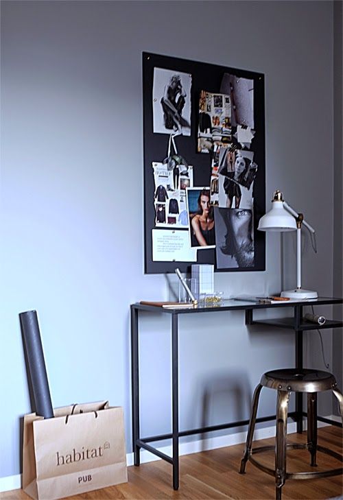 an elegant working space with a black desk that is Vittsjo table, a metal stool, a black memo board with photos and a white table lamp