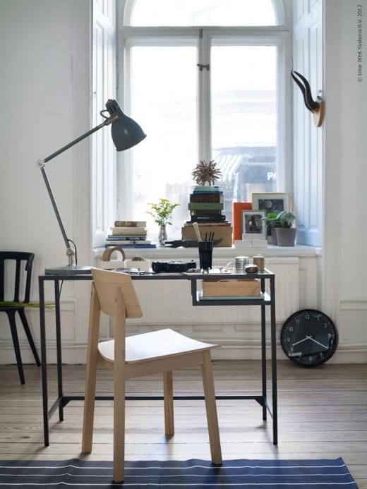 a Nordic working space with a windowsill for storing books, a clock, a black Vittsjo table as a desk, a table lamp and a stained chair