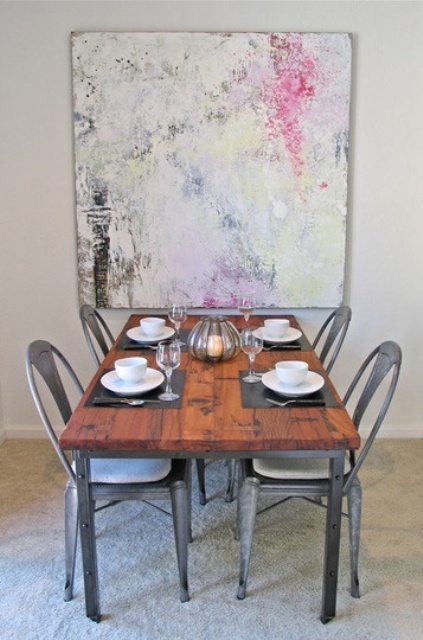 a modern industrial dining space with a wood and metal table, metal chairs, a bright artwork on the wall is a lovely and cool spot for meals