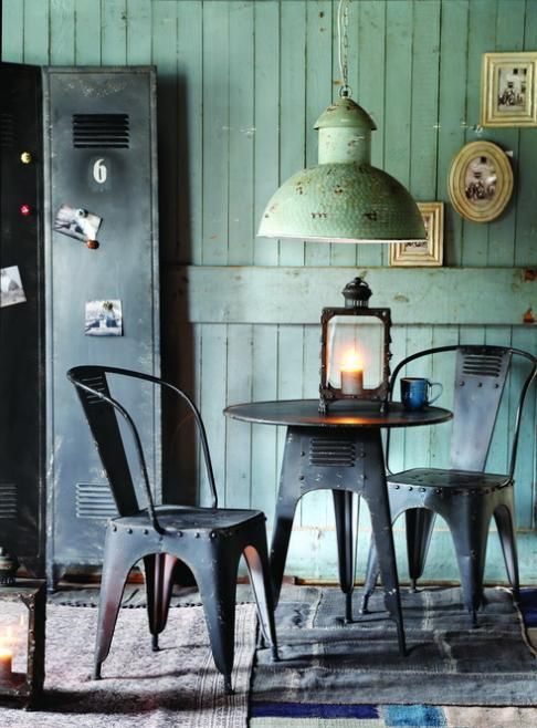 an industrial dining room with green walls, a metal storage unit, a metal round table and matching chairs, a green metal lampshade