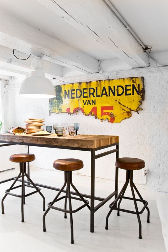 an industrial dining room with a tall table on metal legs and matching industrial stools plus an industrial decoration on the wall